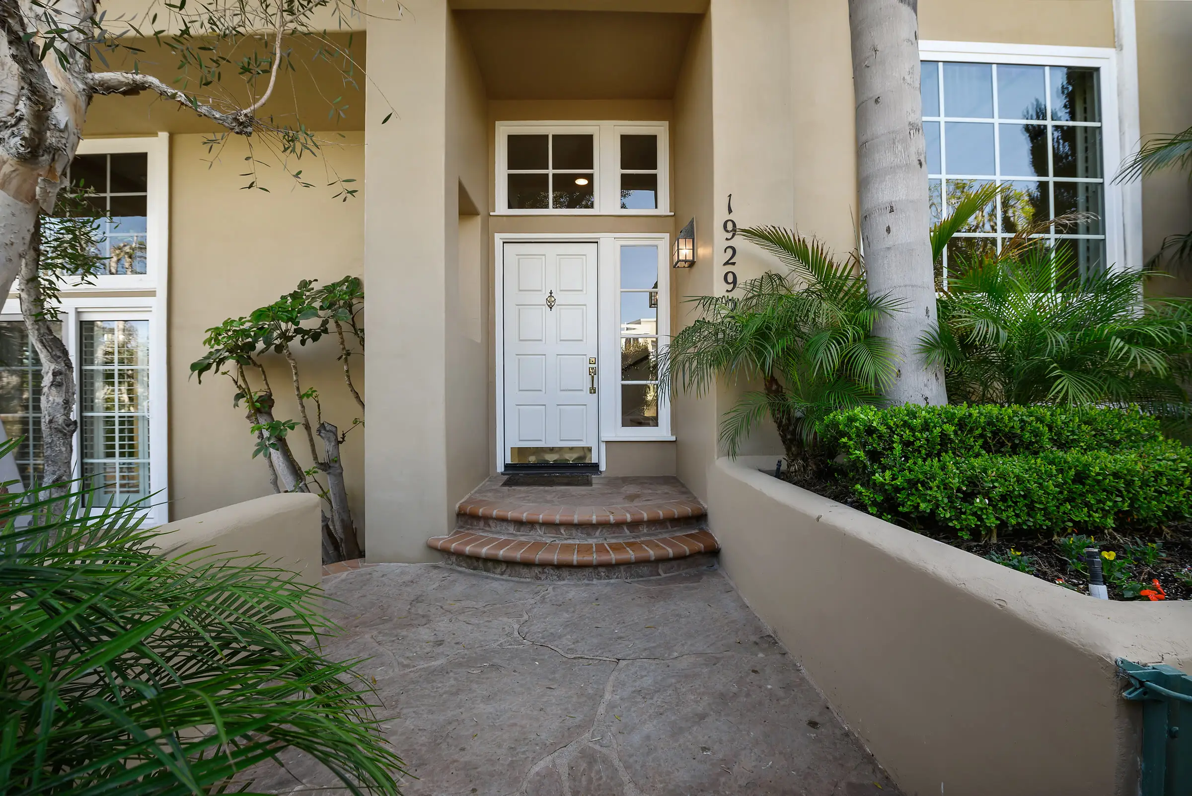 The front entry of an Orange County home: a white six-panel door up three brick steps, palms on either side