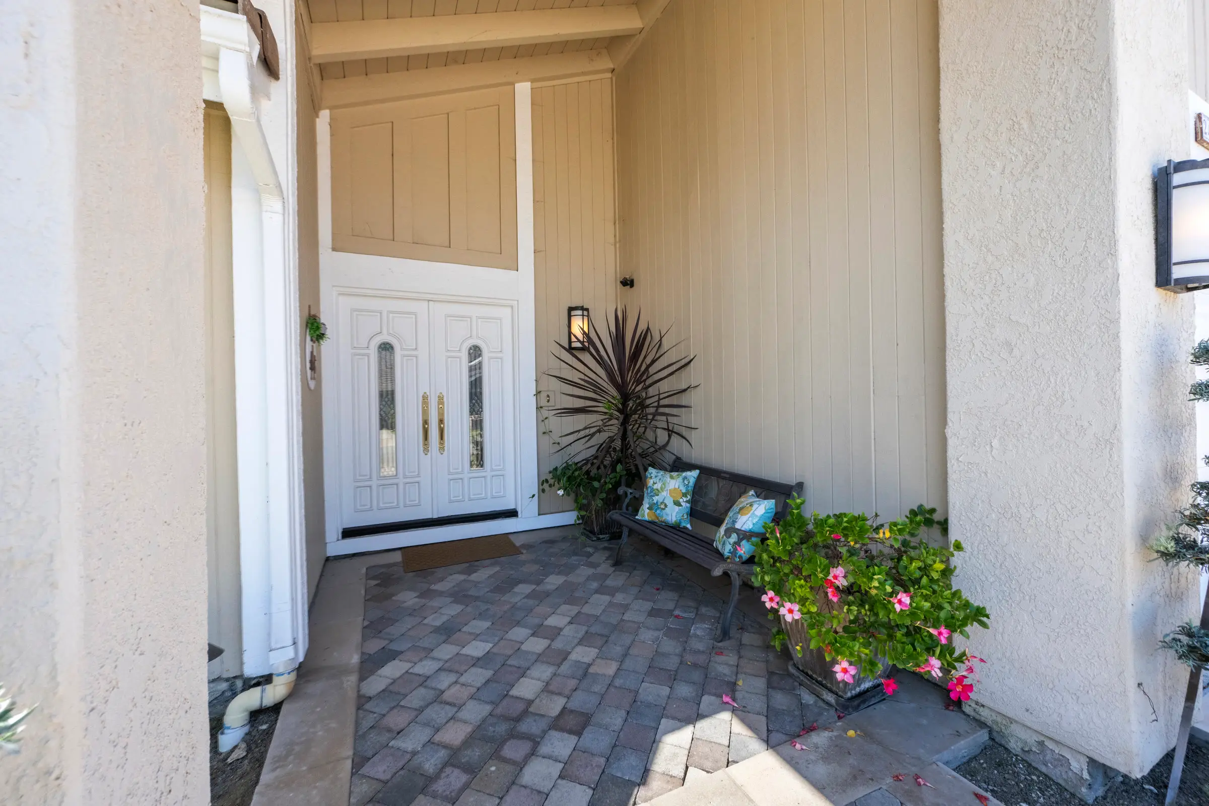 White double front doors under a covered entry, with a bench, cushions and pink flowers