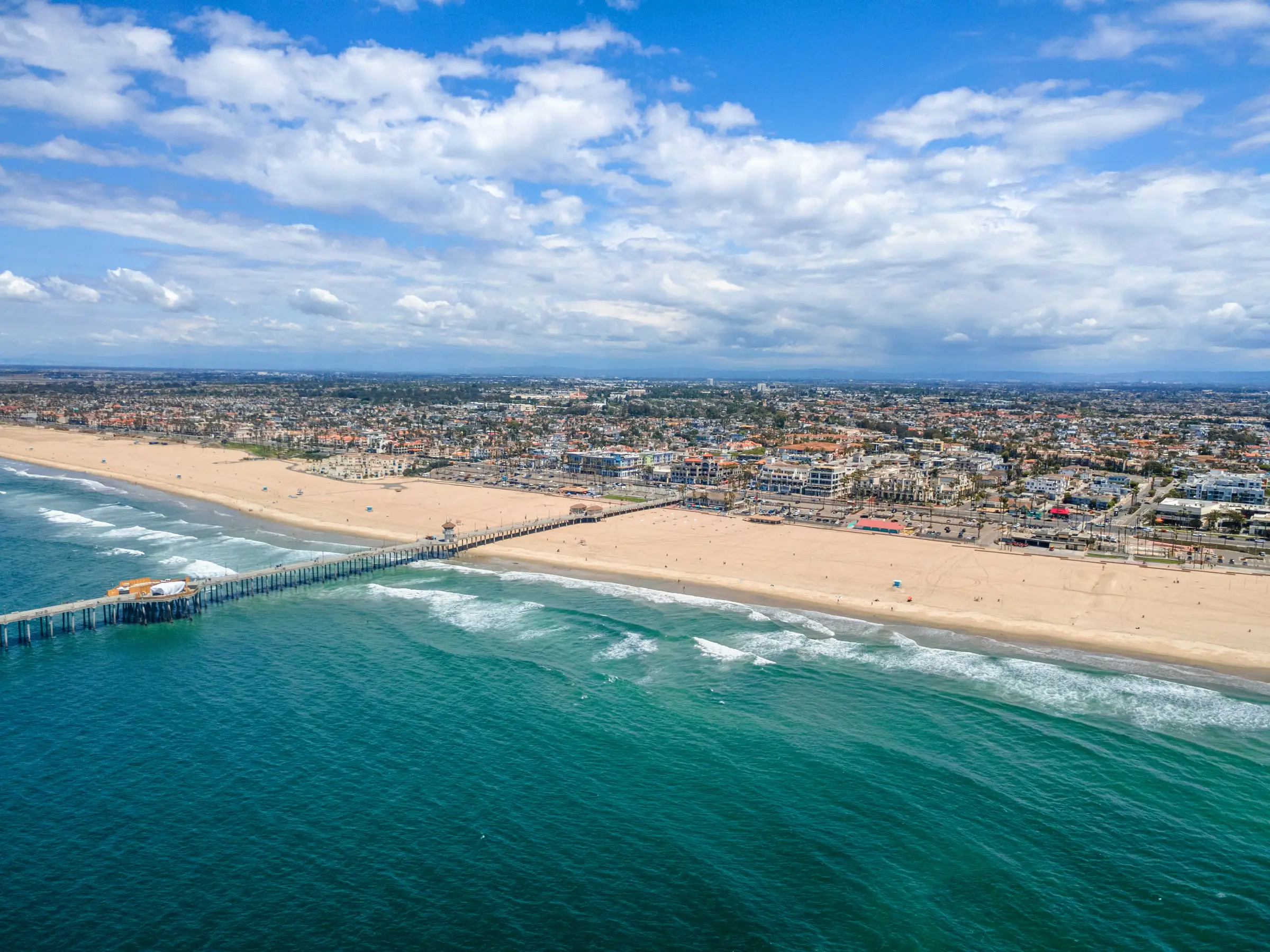 Huntington Beach Pier and the surf line from the air, under a sky of white clouds