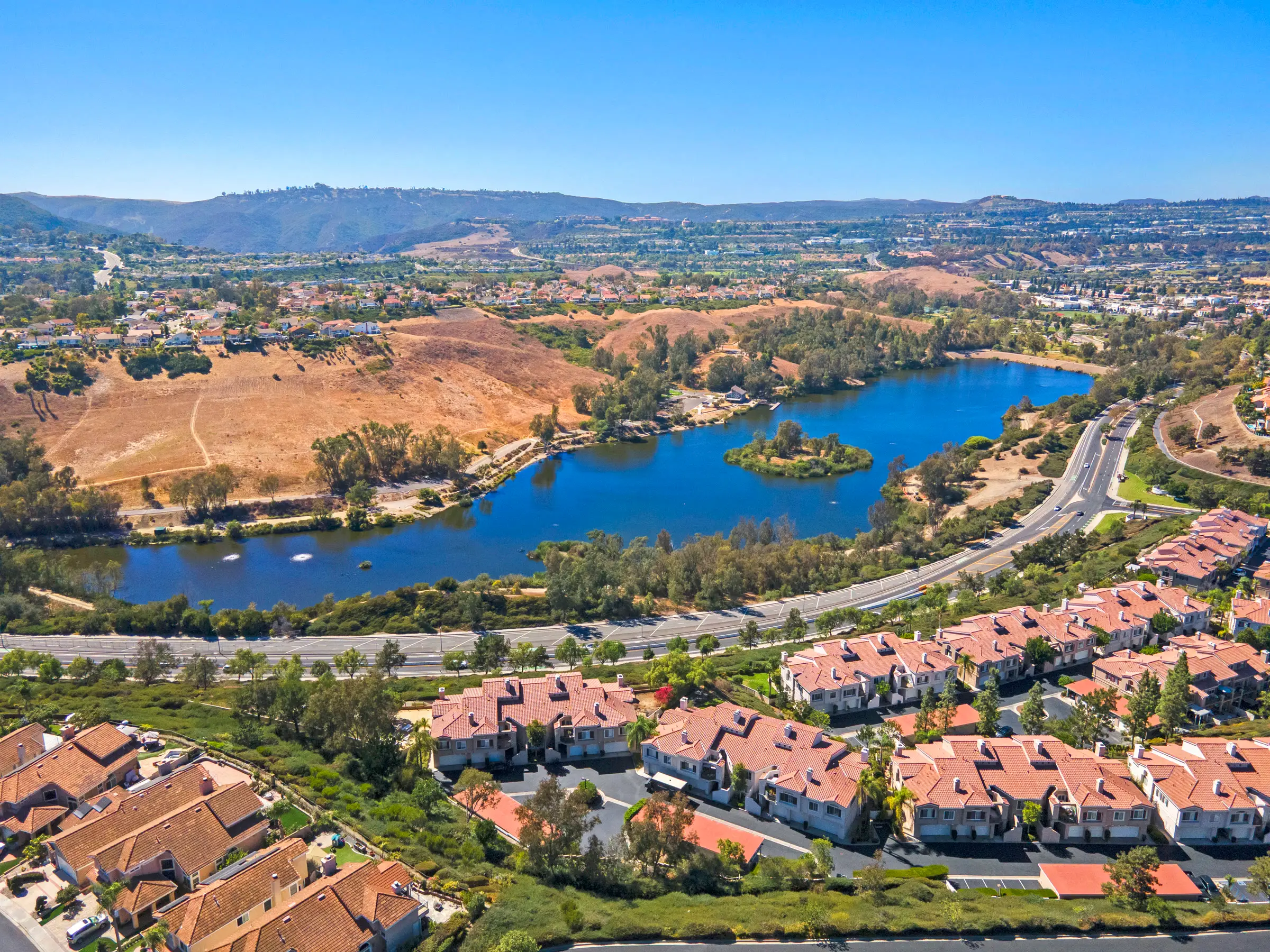 A lake with a small island, golden hills and red-tile homes in Laguna Niguel, from the air