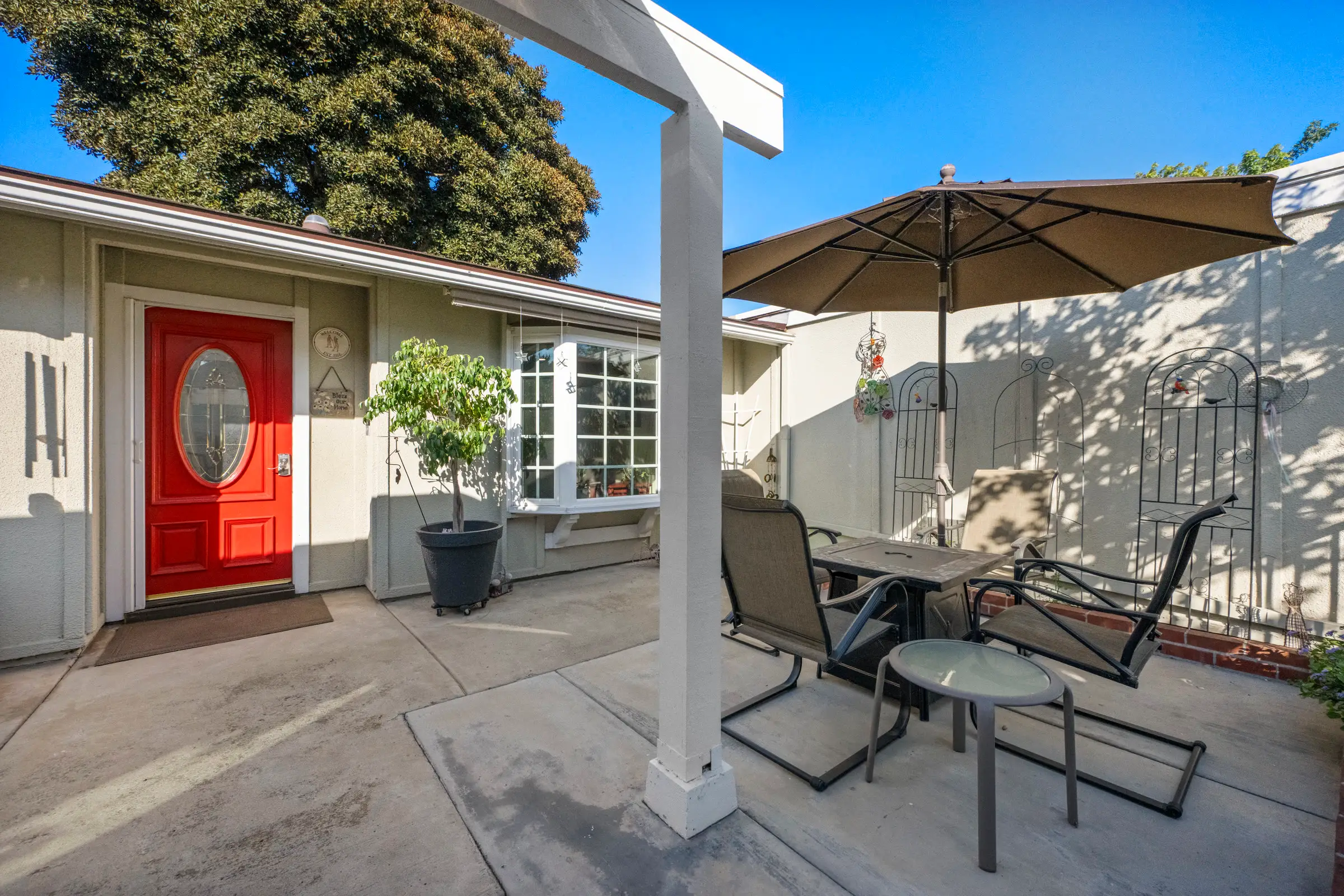 A red front door off a sunny courtyard with a patio table and umbrella